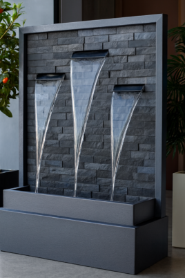 Modern indoor slate water fountain with cascading triangular streams and lush potted plants.