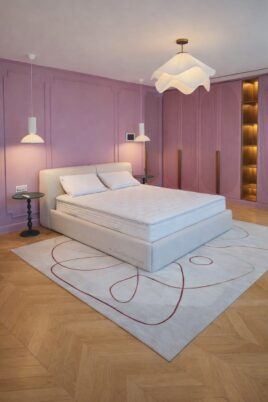 Modern pastel pink luxury bedroom with white upholstered bed, designer lighting, and herringbone wood flooring.